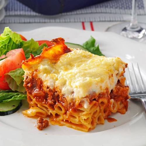 A plate of lasagna with a golden top, served alongside a fresh salad of greens and tomatoes.