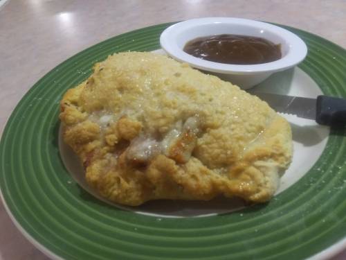 A golden-brown calzone on a plate with a small bowl of dipping sauce.