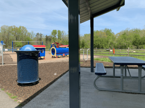 A playground with colorful equipment and a picnic area, surrounded by trees under a clear blue sky.