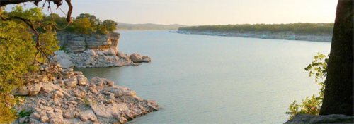 A serene river scene with rocky banks and lush greenery under a soft sunset glow.