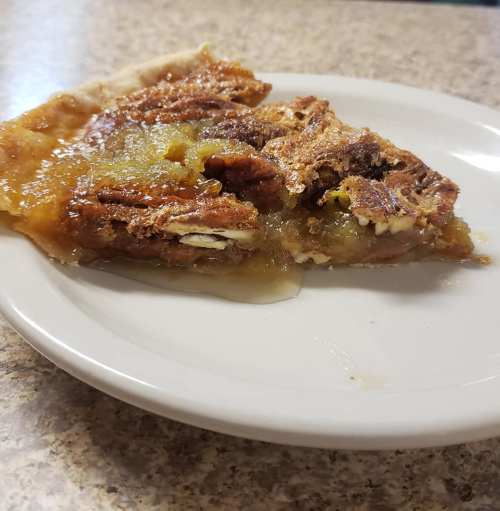 A slice of pecan pie on a white plate, featuring a golden, gooey filling and a flaky crust.