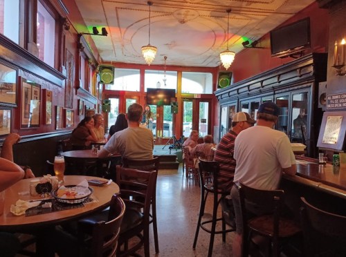 A cozy bar scene with patrons seated at the counter, a stage in the background, and warm lighting.