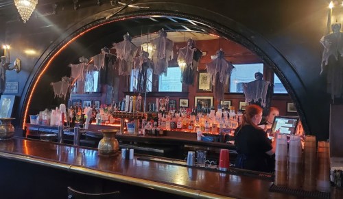 A dimly lit bar with ghost decorations hanging from the ceiling and a bartender serving drinks.
