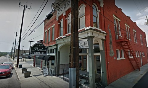 A red brick building with a sign for "Peerless Grille" and outdoor seating, located on a street with power lines.