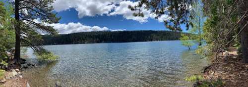 A serene lake surrounded by trees under a partly cloudy sky, with calm water reflecting the landscape.
