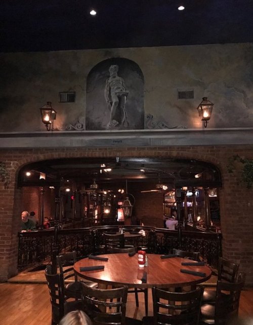 Cozy restaurant interior with brick walls, wooden tables, and a mural of a figure above an arched entrance.