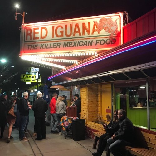 A vibrant restaurant sign reading "Red Iguana" with people gathered outside on a lively street at night.