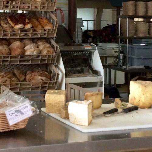 A bakery display with various breads and a cheese cutting station featuring blocks of cheese and a knife.