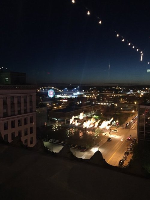 City skyline at night with lights, a ferris wheel in the distance, and a street illuminated below.
