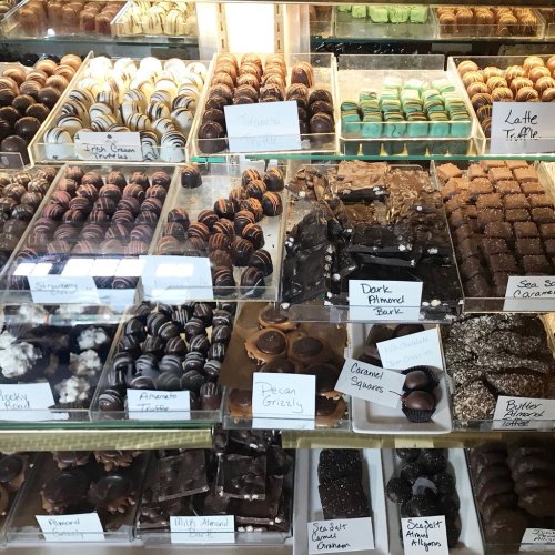 A display case filled with various chocolates and truffles, labeled with flavors like dark almond bark and sea salt caramel.