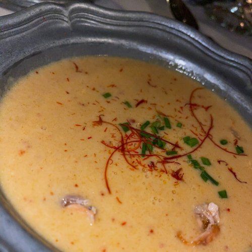 A bowl of creamy soup garnished with saffron strands and chopped herbs, served in an ornate dish.