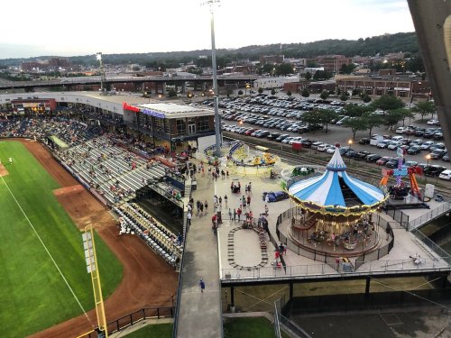 Aerial view of a baseball stadium with a carousel, crowds, and nearby parking lot during an event.