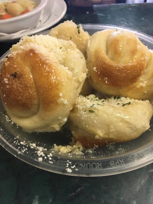 A plate of soft, golden-brown rolls topped with crumbled cheese and herbs, served in a clear plastic container.