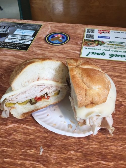 A sandwich with turkey, cheese, and toppings, cut in half on a paper plate, resting on a wooden table.