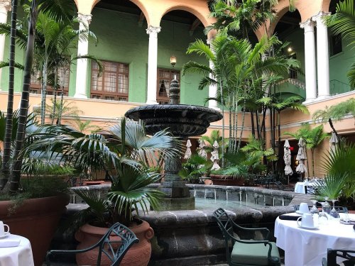 A serene courtyard with a fountain surrounded by lush greenery and elegant columns.