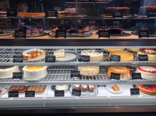 A display case filled with various cakes and desserts, including cheesecakes, tarts, and chocolate treats.