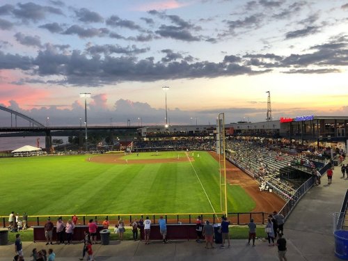 A scenic view of a baseball field at sunset, with spectators in the stands and clouds in the sky.