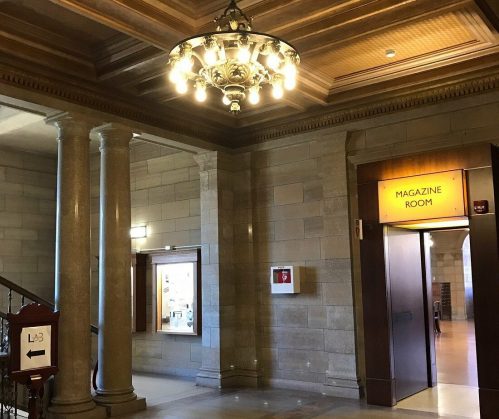 Interior of a building featuring ornate columns, a chandelier, and a doorway labeled "Magazine Room."