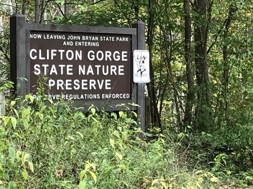 Sign marking the transition from John Bryan State Park to Clifton Gorge State Nature Preserve, surrounded by greenery.