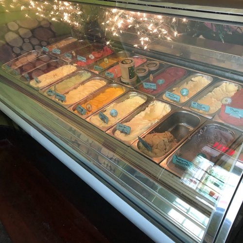 A display case filled with various colorful ice cream flavors in metal tubs, with labels for each flavor.