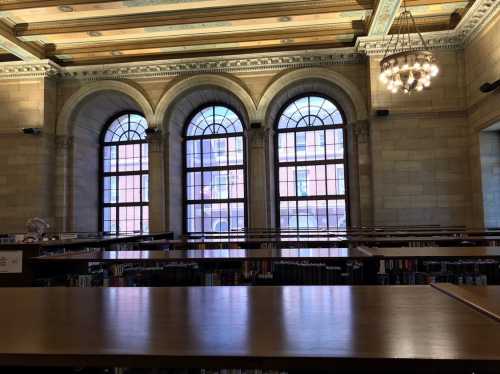 Interior of a library with arched windows, wooden tables, and bookshelves, featuring soft natural light.