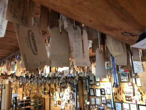 A ceiling filled with hanging tags and labels, surrounded by framed photos on the walls of a rustic interior.