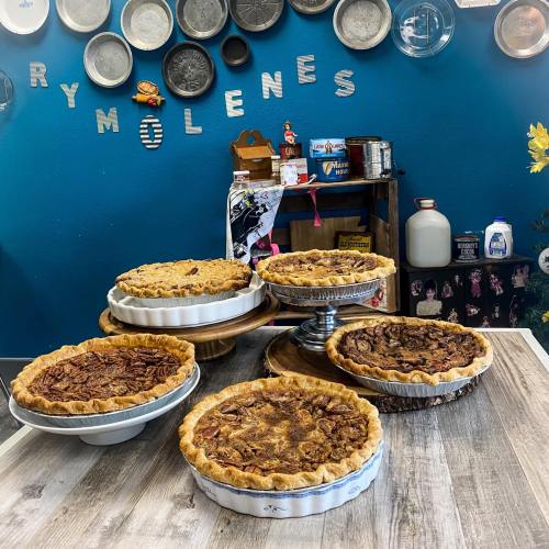 A display of five delicious pies on a wooden table, with a blue wall and decorative plates in the background.