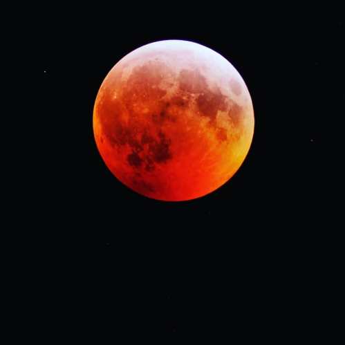 A partially eclipsed moon glowing in shades of orange and red against a dark sky.