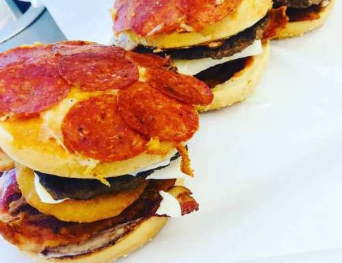 Three stacked sandwiches with layers of pepperoni, cheese, and meat on toasted buns.