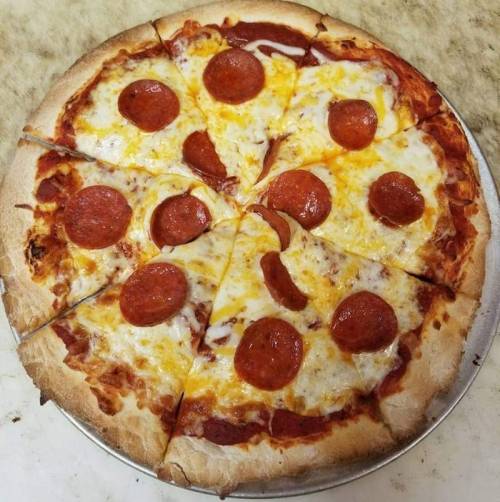 A freshly baked pepperoni pizza with melted cheese, sliced into eight pieces on a silver tray.