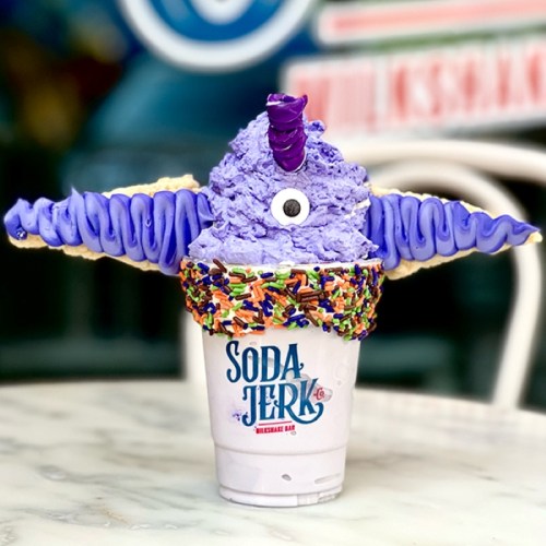 A whimsical purple ice cream creation with sprinkles, resembling a creature, served in a cup labeled "Soda Jerk."