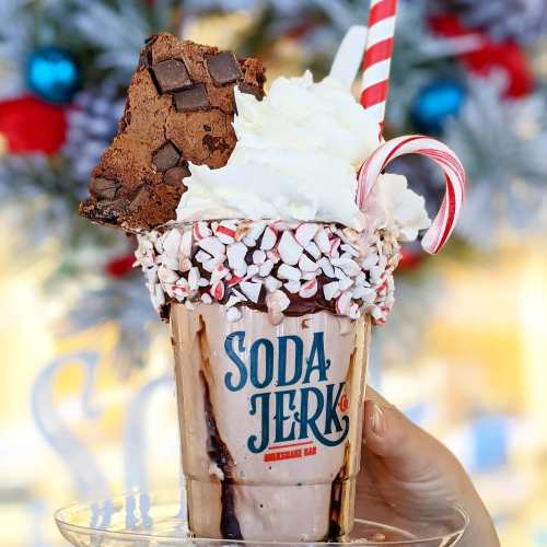 A festive milkshake topped with whipped cream, a brownie, and crushed peppermint, served in a "Soda Jerk" cup.