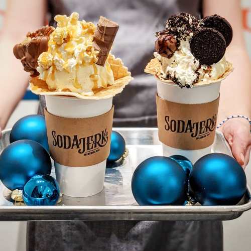 Two festive ice cream cups topped with popcorn, chocolate, and cookies, served on a tray with blue ornaments.