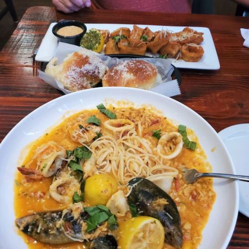 A bowl of seafood pasta with lemon and herbs, alongside a plate of stuffed pastries and dipping sauce.
