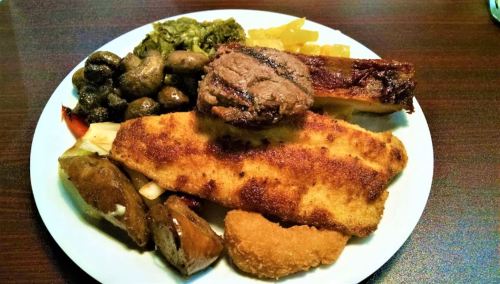 A plate of assorted foods including fried fish, meat, greens, and various sides.