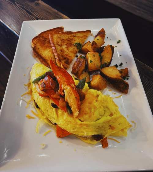 A plate featuring a fluffy omelette topped with vegetables, served with toast and golden-brown roasted potatoes.