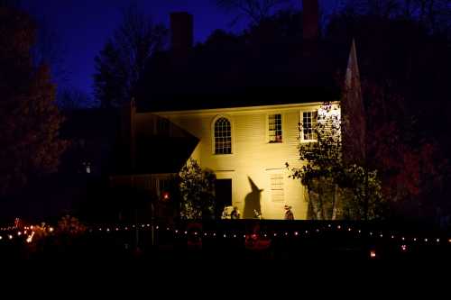 A dimly lit yellow house at night, with a shadow of a figure resembling a witch cast on the wall.