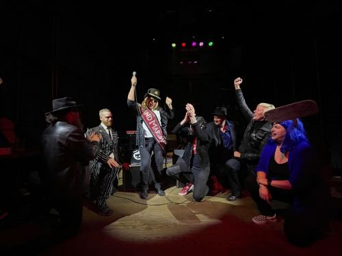 A lively performance scene with a group of entertainers in costumes, celebrating on stage with dramatic poses and expressions.