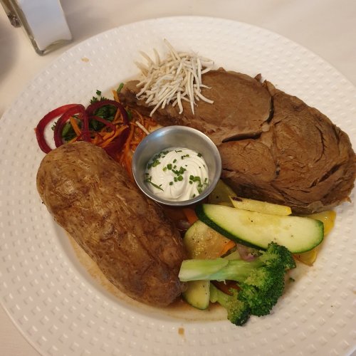 A plate featuring sliced roast beef, a baked potato, mixed vegetables, and a small bowl of sour cream.