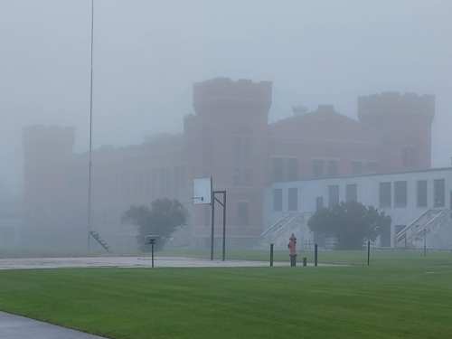 A foggy scene featuring a castle-like building in the background and a basketball hoop in a grassy area.