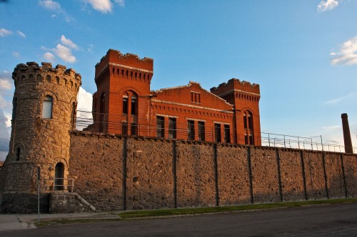 Historic brick building with towers, surrounded by a stone wall, under a blue sky with scattered clouds.