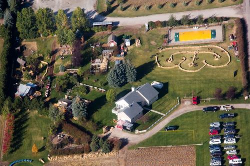 Aerial view of a rural property with a house, maze, sports court, and parked cars in a scenic landscape.