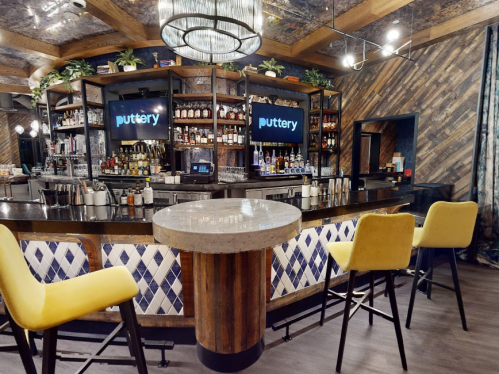 A stylish bar with a circular counter, yellow stools, and shelves stocked with various bottles in a modern setting.
