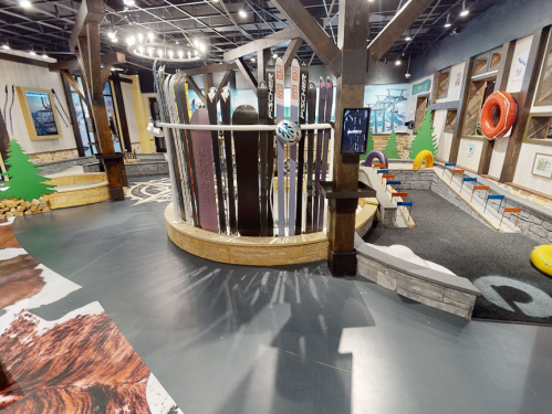 A spacious indoor area featuring ski equipment displays, colorful seating, and playful decor elements like trees and tires.