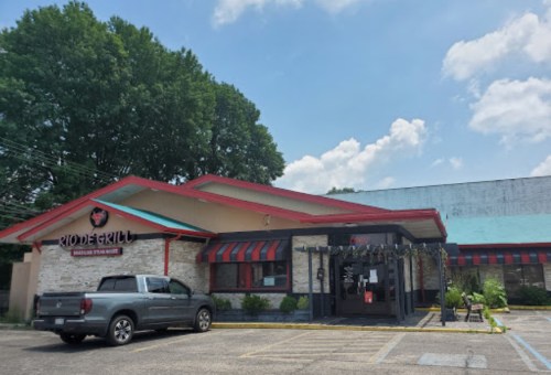 Exterior of a Brazilian steakhouse with a red roof, parked truck, and blue sky with clouds in the background.