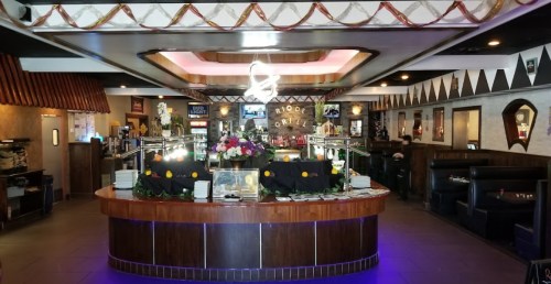 Interior of a restaurant featuring a buffet area with floral decorations and seating booths in a vibrant atmosphere.