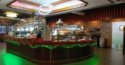 A buffet counter with metal food trays, decorative plants, and green lighting in a warmly lit restaurant interior.