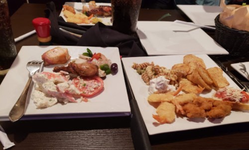 Two plates of food: one with shrimp, salad, and chicken; the other with pasta, fried shrimp, and breaded items.