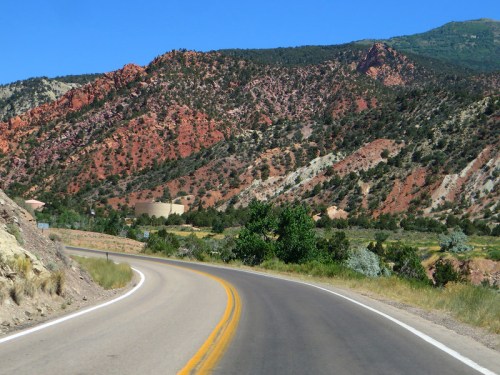 A winding road curves through vibrant red and green mountains under a clear blue sky.