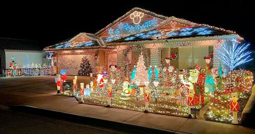 A brightly lit house decorated for Christmas with colorful lights, trees, and festive figures in the yard.